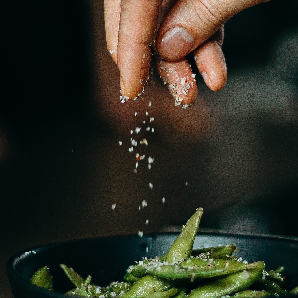 person-pouring-seasoning-on-green-beans-on-bowl-3338497
